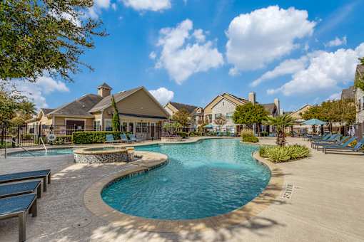A large outdoor swimming pool surrounded by lounge chairs and trees.