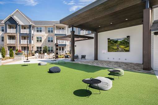 A patio area with a green lawn and a white wall with a picture on it.