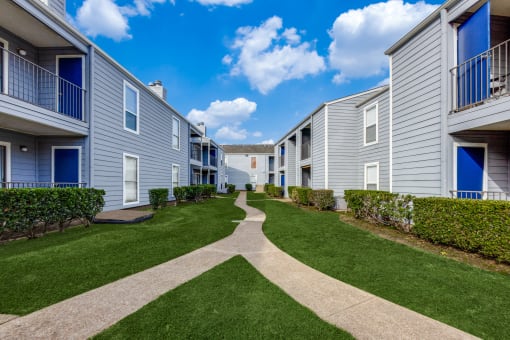 a walkway between two apartment buildings with green grass