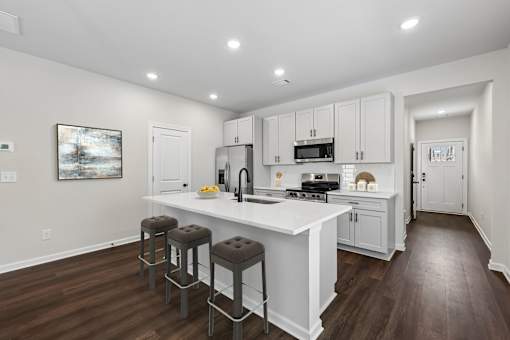 A kitchen with white cabinets and a white island with three stools.
