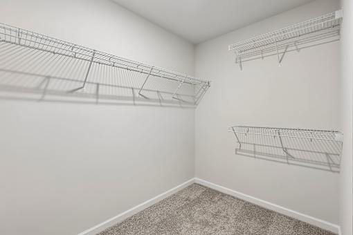 A white wall with three empty wire shelves.