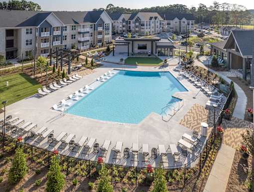 A large swimming pool surrounded by lounge chairs and a fence.