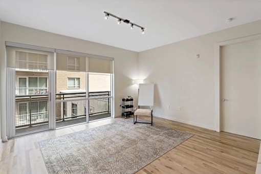 A room with a rug, a chair, and a window with a view of a balcony.