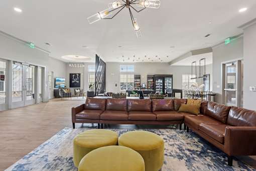 A large brown leather couch is in the middle of a spacious room with a chandelier hanging from the ceiling.