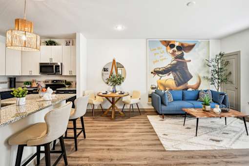 A modern kitchen with a bar area and a living room with a sofa and a painting of a dog.