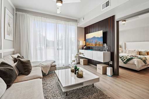 A modern living room with a large window, a sofa, a coffee table, and a bed.