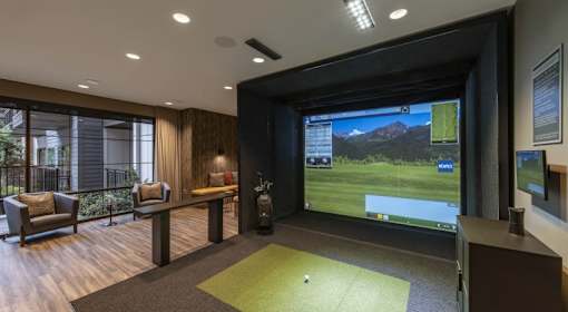 A room with a golf simulator screen and a green carpet.