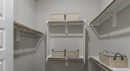 A white closet with three shelves and baskets on them.