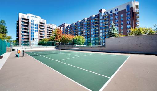 A tennis court is surrounded by apartment buildings.