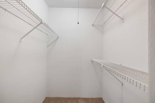 a walk in closet with white walls and shelves and a wire rack on the wall