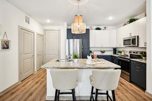 A kitchen with a granite countertop and two chairs.