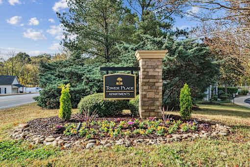 A sign for Tower Place Apartments is surrounded by flowers and greenery.