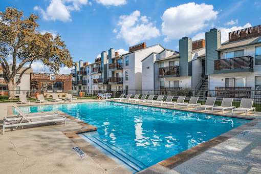 A swimming pool surrounded by lounge chairs and buildings in the background.
