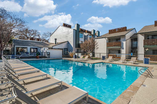 A swimming pool with sun loungers in front of apartment buildings.