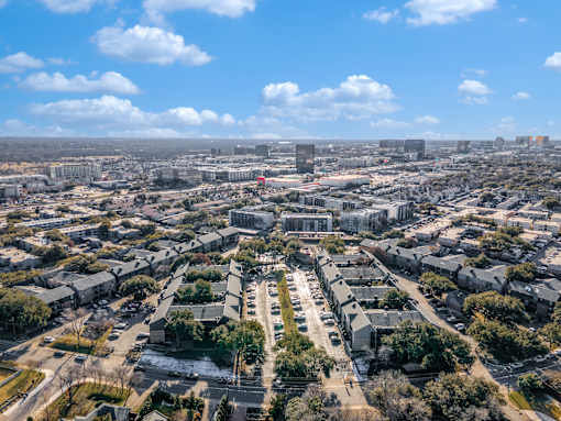 A cityscape with buildings and roads under a blue sky with clouds.