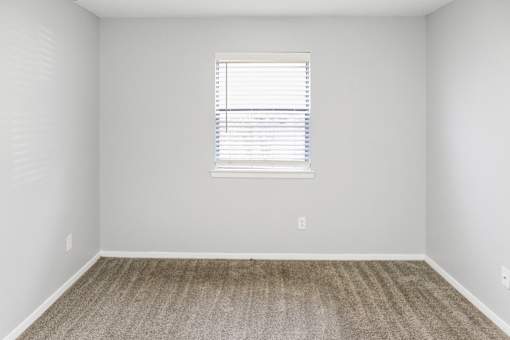 A room with a carpeted floor and a window with blinds.