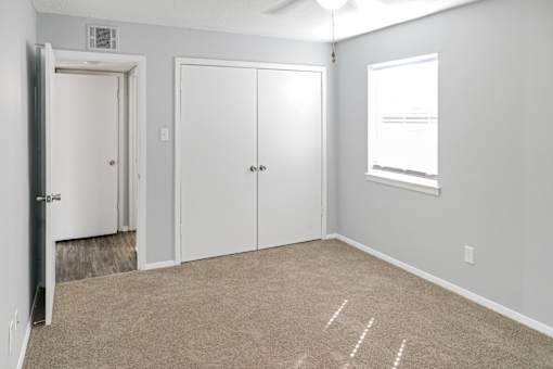 A room with a carpeted floor, two doors, and a window.