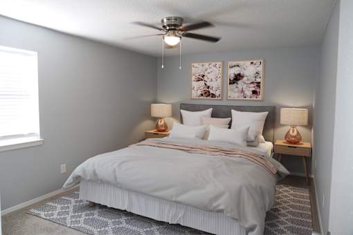 A bedroom with a bed, two lamps, and a ceiling fan.
