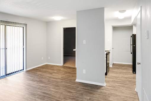 A spacious living room with a black refrigerator and wooden flooring.