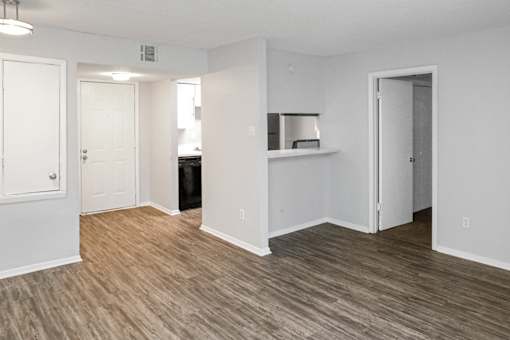 A room with white walls and wood flooring with a door on the left and a shelf on the right.