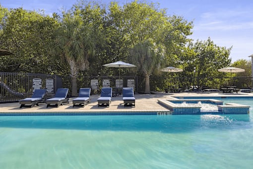 A pool with a waterfall and a row of sun loungers.