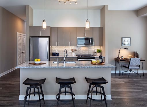 A modern kitchen with a bar area and three stools.