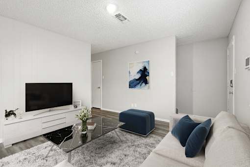 A modern living room with a flat screen TV, a glass coffee table, and a blue ottoman.