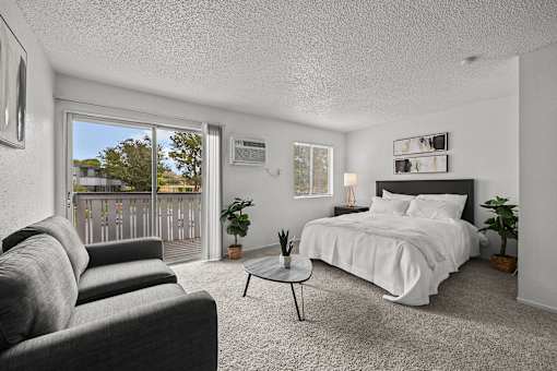 A bedroom with a large bed, grey couch, and a small table.