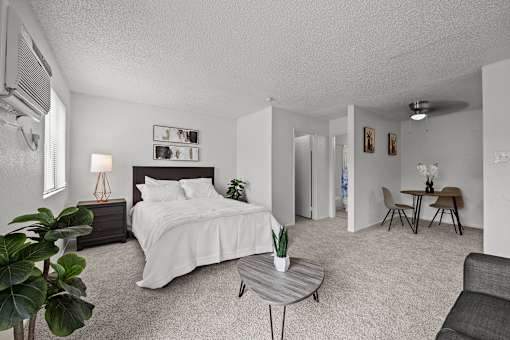 A bedroom with a bed, a couch, a table, and a plant.