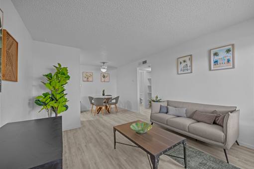 A living room with a grey couch, a wooden coffee table, and a dining table with chairs.