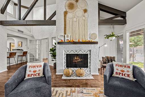 A living room with a fireplace and two grey armchairs with pillows that say pumpkin spice.