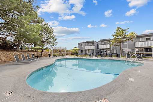 A large outdoor swimming pool surrounded by trees and a building in the background.