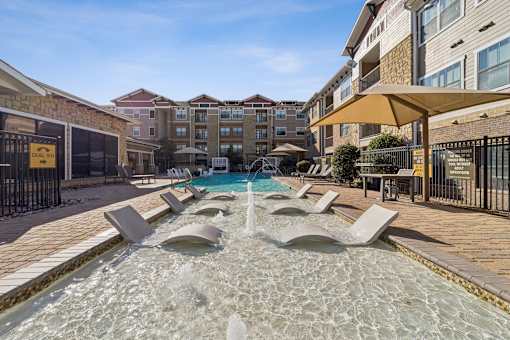 A fountain in the middle of a pool surrounded by lounge chairs.