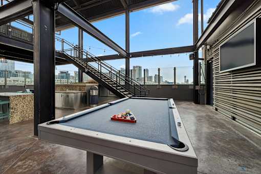 A pool table with a red cloth and a white cue ball is in the foreground of an outdoor pool hall.
