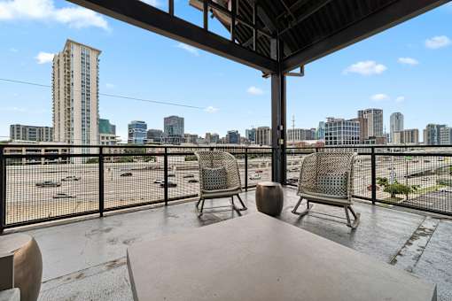 A balcony with two chairs and a table overlooking a city skyline.