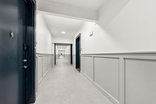 A long hallway with white walls and a black door on the left.