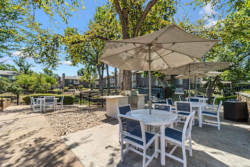A patio with white chairs and tables under umbrellas.