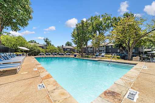 A large swimming pool surrounded by trees and lounge chairs.