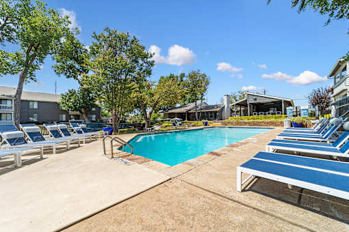 A pool surrounded by sun loungers and trees.