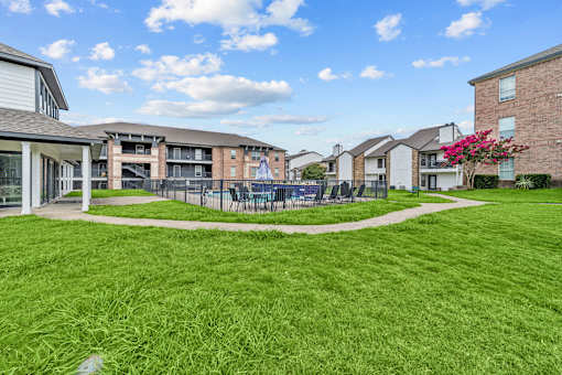 A grassy area in front of apartment buildings with a pink flowering bush.