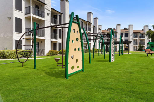 a playground with a climbing wall and monkey bars in front of an apartment building