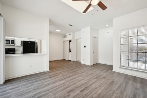 an empty living room with a ceiling fan and a kitchen