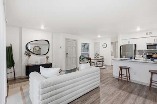 A white couch is in the middle of a living room with a kitchen in the background.