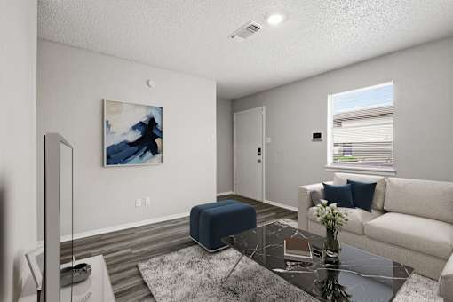 A living room with a blue ottoman, a white couch, and a painting on the wall.