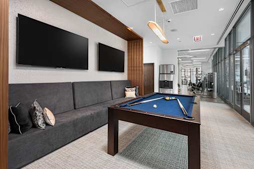 A pool table in a room with a couch and two TVs.