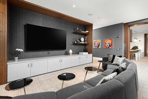 A modern living room with a grey sofa, a black chair, and a flat screen TV mounted on the wall.