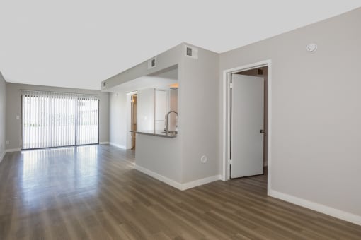 the living room and kitchen of an empty apartment with wood floors and white walls