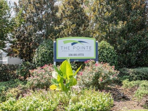 a sign for the pointe in a garden with bushes and trees