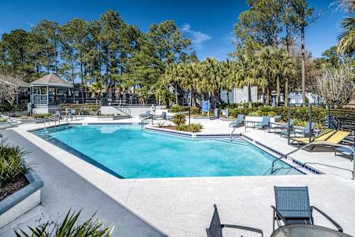 A swimming pool surrounded by trees and chairs.