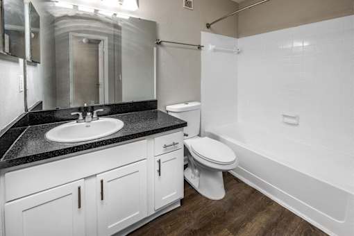 A white toilet sits in a bathroom with a black counter top.
